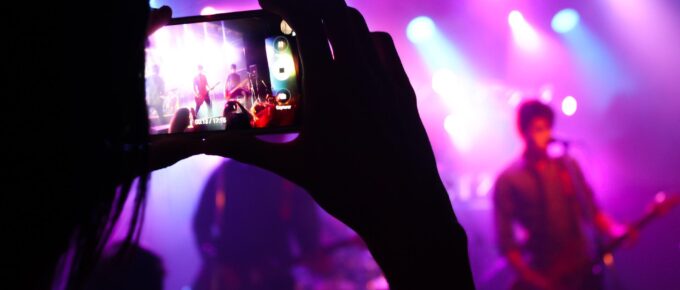 Person at rock concert with pink strobe light records musician on stage from crowd on phone